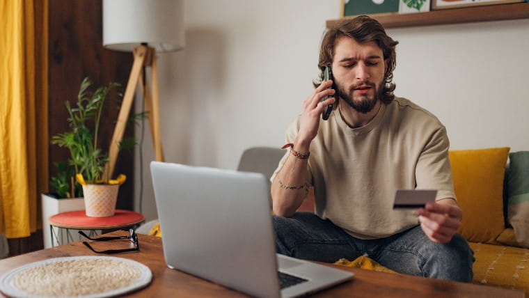 Young man reading credit card information while on phone.