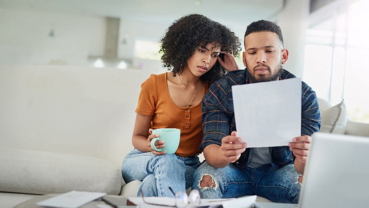 Couple sitting on couch reading bills.