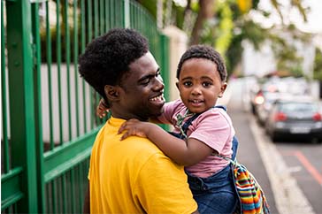 Father holding his child as they walk down the street.