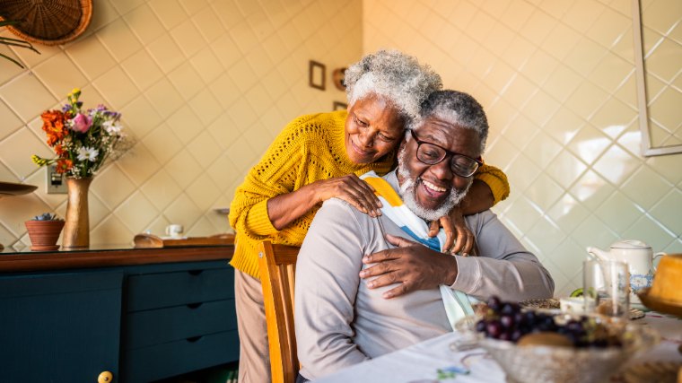 Senior couple hugging at table.